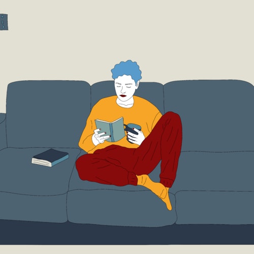 Person sitting on the couch drinking coffee and reading a book