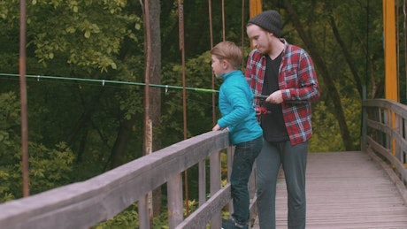 A boy and a man fishing on a bridge in nature.
