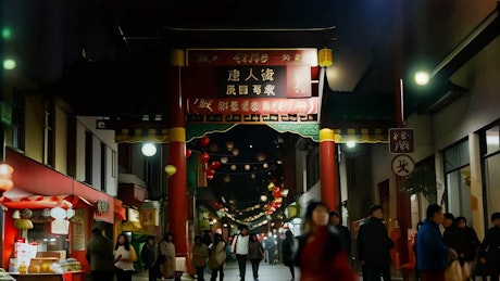 夜晚，一条繁忙的街道上装饰着中国的灯光，几个人走在一扇传统的中国门下