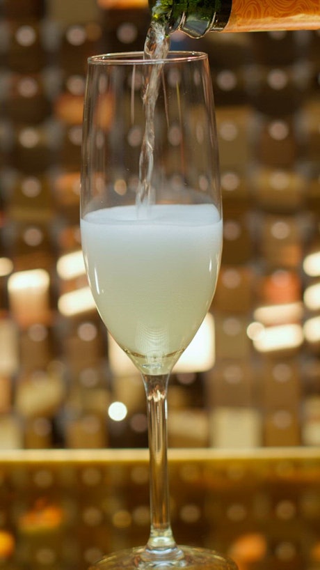 A champagne bottle fills up a flute glass till the foam reaches the top and spills.