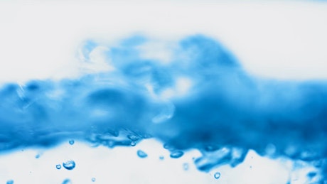 A close up shot of blue water bubbles reaching the surface over a white background.