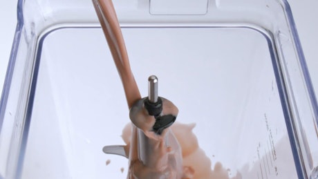 A continuous stream of chocolate milk fills a transparent blender.
