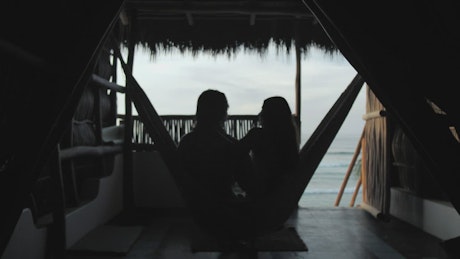 A couple in a hammock at a beach hut.