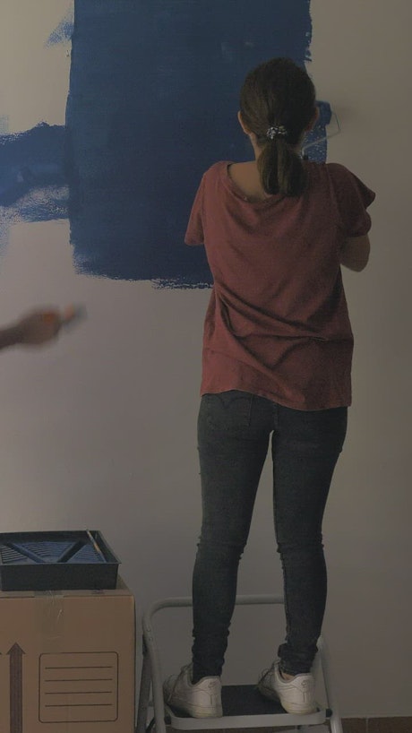 A couple painting a wall blue.