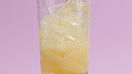 A crystal glass with ice fills up with effervescent orange  soda.