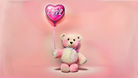 一只可爱的泰迪熊拿着一个写着“爱”的心形气球，在粉红色的背景上行走