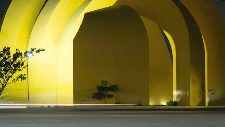 A fast timelapse of the street with a monumental yellow arches sculpture in the background.