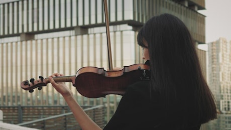 A female violinist playing music on a rooftop.