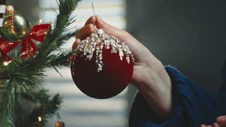 A girl's hand puts a sphere on the Christmas tree.