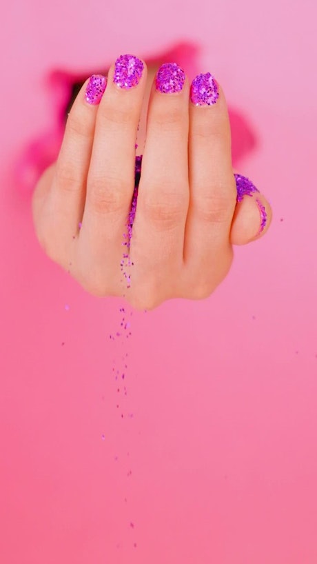 A girl's hand spilling glitter on a pink background.