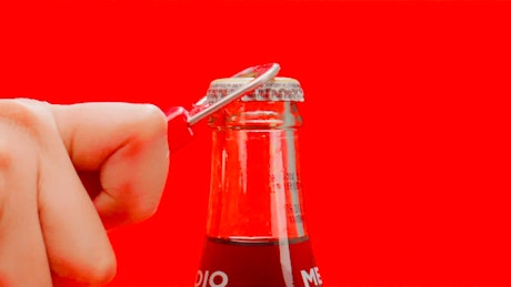 A glass bottle of soda being opened with a retro soda opener.