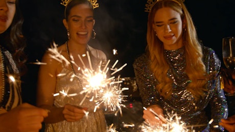 A group of friends donned with elegant dresses and suits light up celebratory sparklers for New Year's Eve.