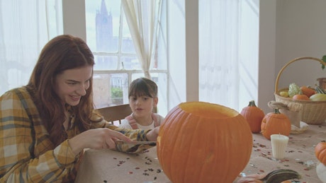 A Halloween pumpkin being made by a mother and daughter.