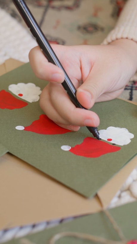 A hand adds eyes to a Santa Claus illustration on a green paper.