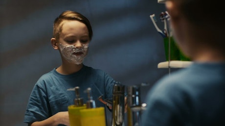 A little boy is shaving in front of the mirror