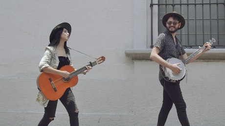 A man and a woman walking down the street playing music