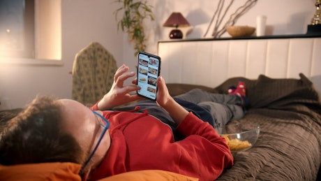 A man lying on the bed scrolling on his phone