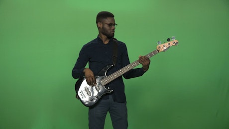A man playing a black guitar and a greenscreen.