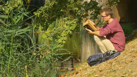 A man reading a book by the river