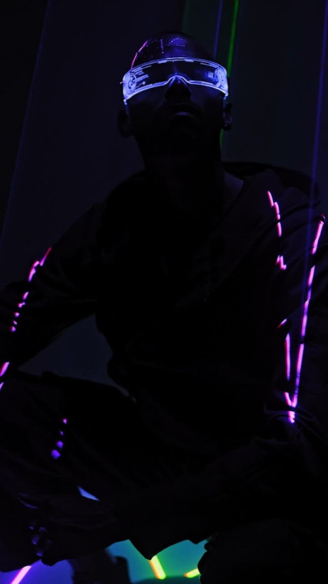 A man sitting beneath laser lights in cyberpunk glasses.