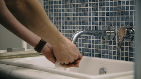 A man washes his face in the bathroom sink.