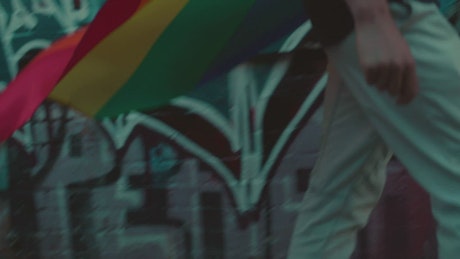 A man with a rainbow flag walking in the street.