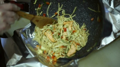 A noodle dish is poured into a takeaway container.