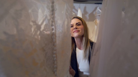 A pair of young woman browse trough white beautifull bride dresses in a wardrobe.