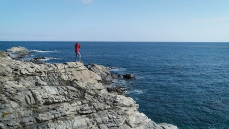 A person taking pictures standing on a cliff.