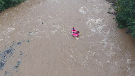 A pink boat rafting in a wild river.