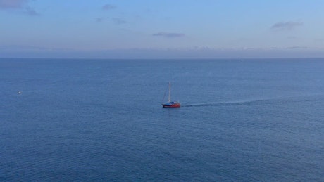 A sailboat sailing through the blue sea, aerial view.