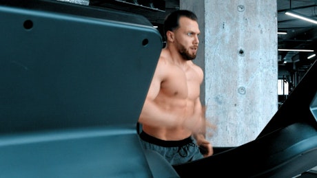 A shirtless man running in the gym.