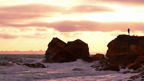 A silhouette of a  person over a rock in the seashore at sunset
