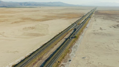 A steady stream of trucks and vehicles traversing the expansive highway in the middle of the arid landscape.