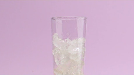 A stream of soda fills up a crystal glass with ice.