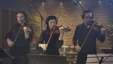 A trio of violinists performing in a recording studio.