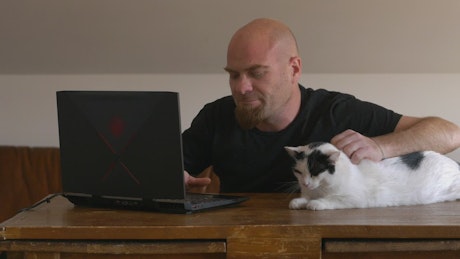 A white cat sits on a desk watching his man work.