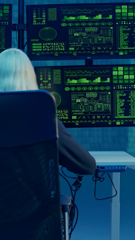 A white-haired man in front of computer monitors with code patterns.
