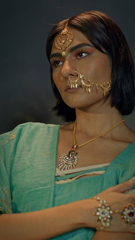 A woman adorned with jewelry on her hand and face striking a pose.