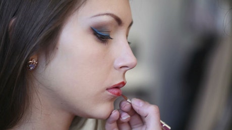A woman is applying lipstick on model.