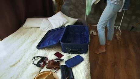 A woman throws clothes haphazardly into an open suitcase.