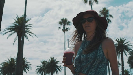 A woman walking and drinking a smoothie.