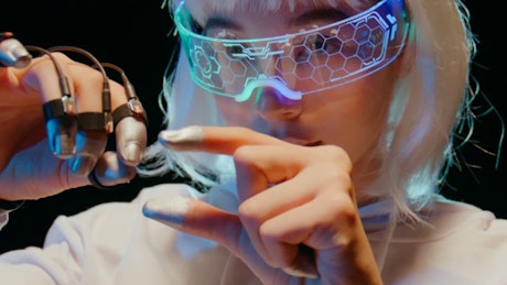 A woman wearign a futuristic VR glasses concentrates on the moves  of her hands to control an unseen user interface.