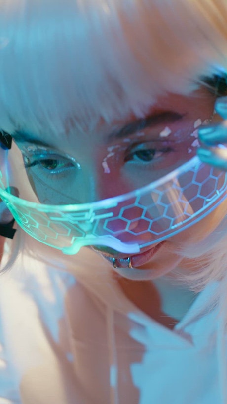 A woman with white hair puts on futuristic looking glasses with a hexagonal patern and RGB lights.