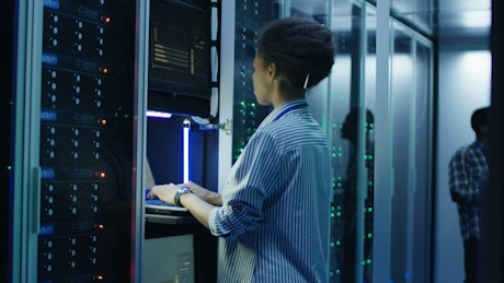 A woman working with a computer in the server room.