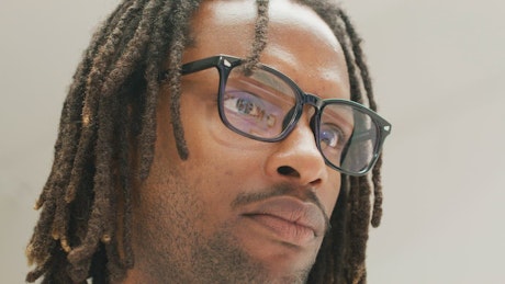 A young Afro-American man with dreadlocks and glasses looking at the computer screen.