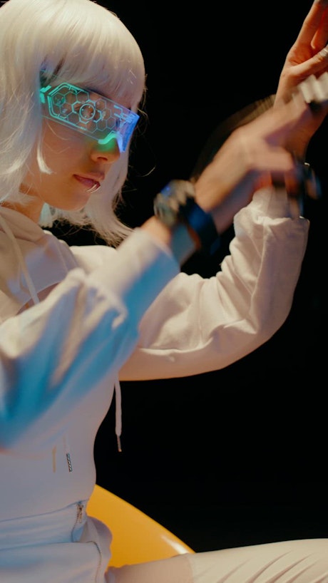 A young beautiful woman wearing a white suit, futuristic VR glasses and a sci fi device on her hands moves fluidly in the digital realm.