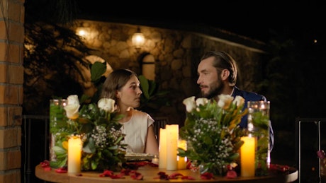 A young couple engages in conversation at a romantic adorned table with roses and candles.