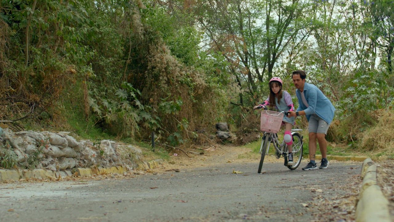 A young father carefully assists his daughter as she learn to ride a bike - Free Stock Video