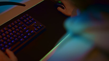 A young man gaming constantly pressing the backlit keyboard.